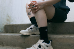 Chaussettes Strata en coton noir avec logo Module 48, portées avec des baskets claires, sur des marches en béton