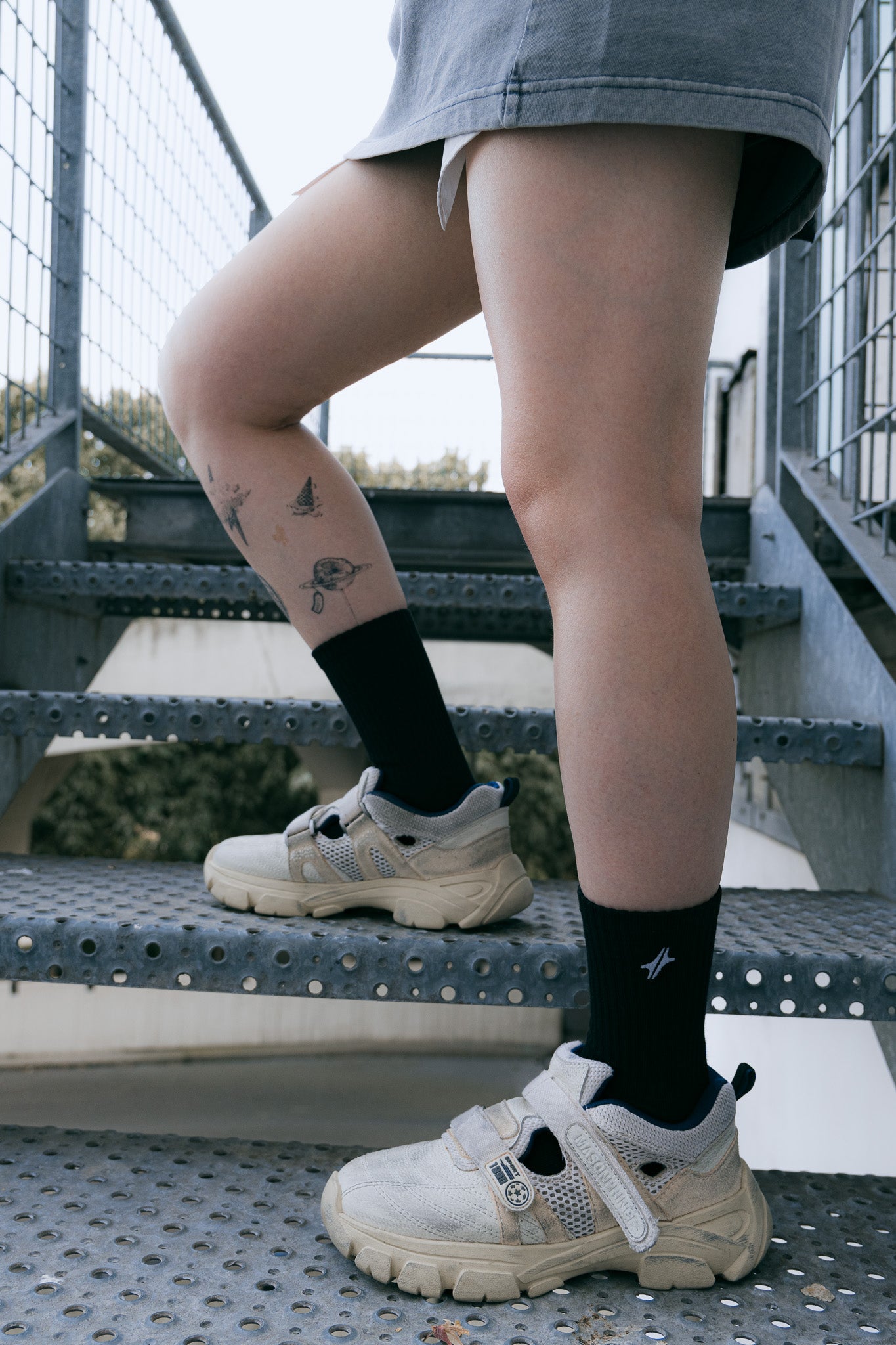 Chaussettes Strata en coton noir avec logo Module 48, portées avec des baskets claires sur un escalier métallique