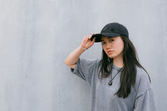 Casquette Drift en coton anthracite délavé, portée, main sur la visière, devant un mur en béton clair