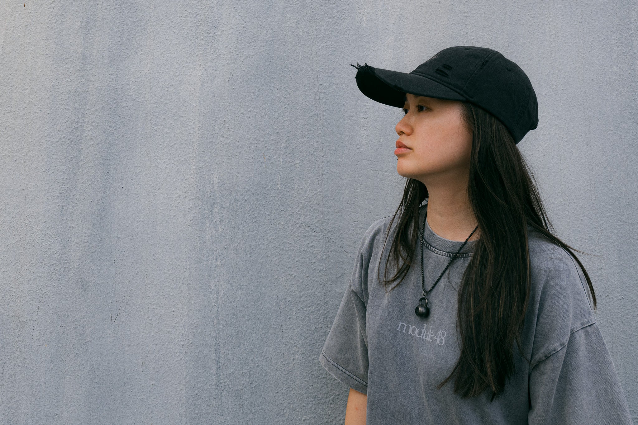 Casquette Drift en coton anthracite délavé, portée avec un t-shirt gris, devant un mur en béton clair